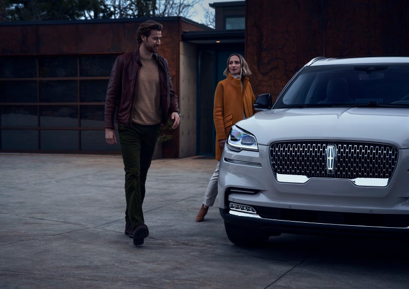A man and a woman approaching a 2024 Lincoln Aviator® SUV, which illuminates certain lights when they are close | Boulevard Lincoln in Georgetown DE