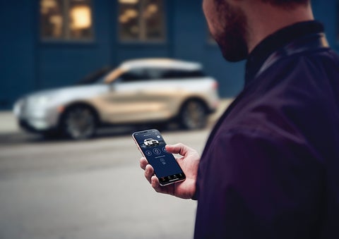 A person is shown interacting with a smartphone to connect to a Lincoln vehicle across the street. | Boulevard Lincoln in Millsboro DE
