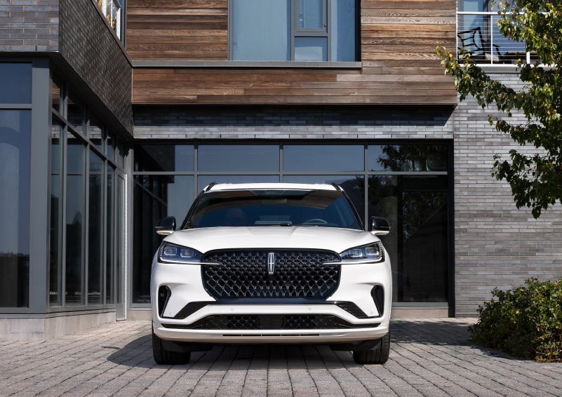 A white 2025 Lincoln Aviator® SUV is shown parked outside a modern building with gray brick and wood accents. | Boulevard Lincoln in Millsboro DE