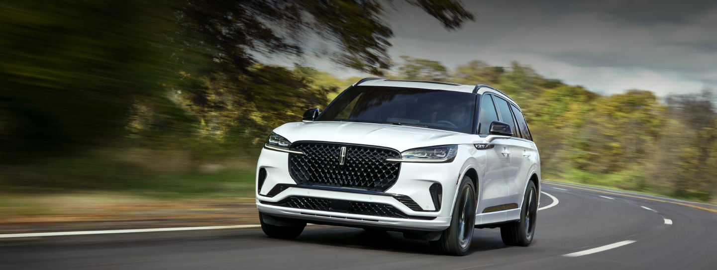 A white 2025 Lincoln Aviator® SUV is being driven down a road lined with trees. | Boulevard Lincoln in Millsboro DE