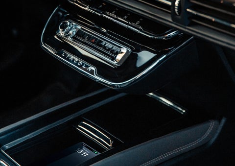A smartphone rests on the wireless charging pad in the front center console cubby.