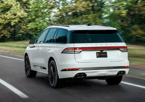 A white 2026 Lincoln Aviator® SUV is being driven away down a road lined with colorful trees. | Boulevard Lincoln in Millsboro DE