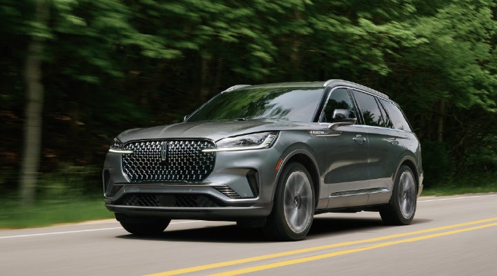 A 2027 Lincoln Aviator® SUV is being driven down a road lined with trees. | Boulevard Lincoln in Millsboro DE